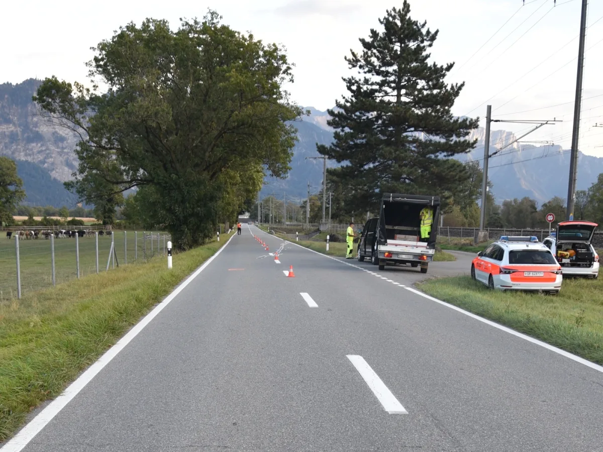 Ein Polizeifahrzeug und ein weiteres Fahrzeug am rechten Rand einer Landstraße, Absperrkegel blockieren die Fahrbahn. Zwei Personen in Arbeitskleidung stehen neben den Fahrzeugen.