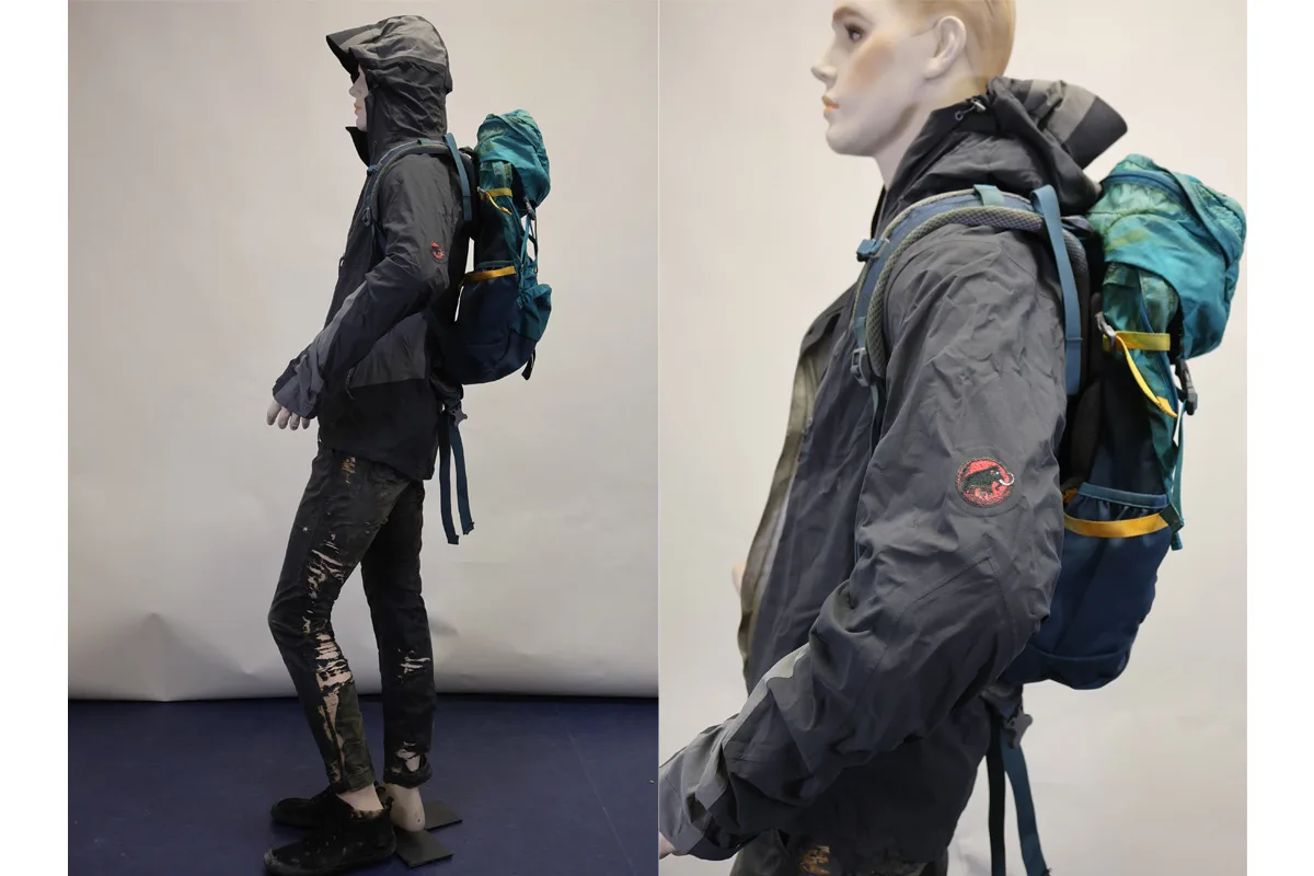 Eine Schaufensterpuppe ist mit einer dunklen Outdoor-Jacke und einem blauen Rucksack bekleidet. Sie steht seitlich und zeigt die Details der Ausrüstung.