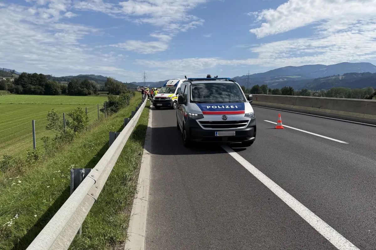 Ein Polizeifahrzeug und weitere Einsatzfahrzeuge stehen auf einer Autobahn. In der Ferne sind Berge zu sehen.