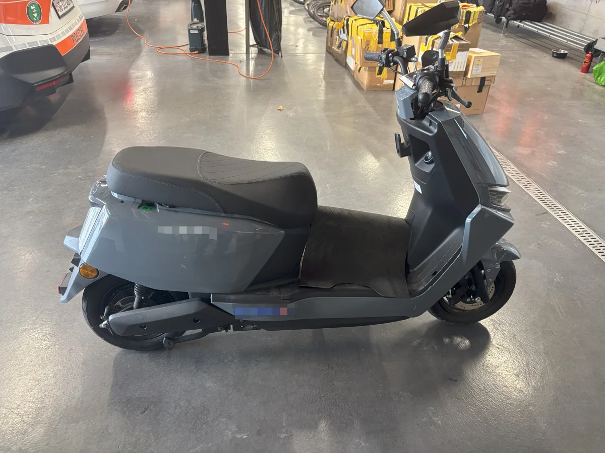 Ein grauer Motorroller steht in einer Garage neben einem Polizei-Pkw. Im Hintergrund sind Kartons zu sehen.
