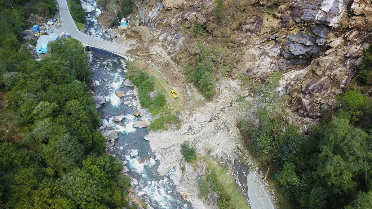 Ein gelbes Auto steht zwischen Geröll, das von einem Erdrutsch auf eine enge Straße einer Bergregion gefallen ist. Ein Fluss fließt daneben.