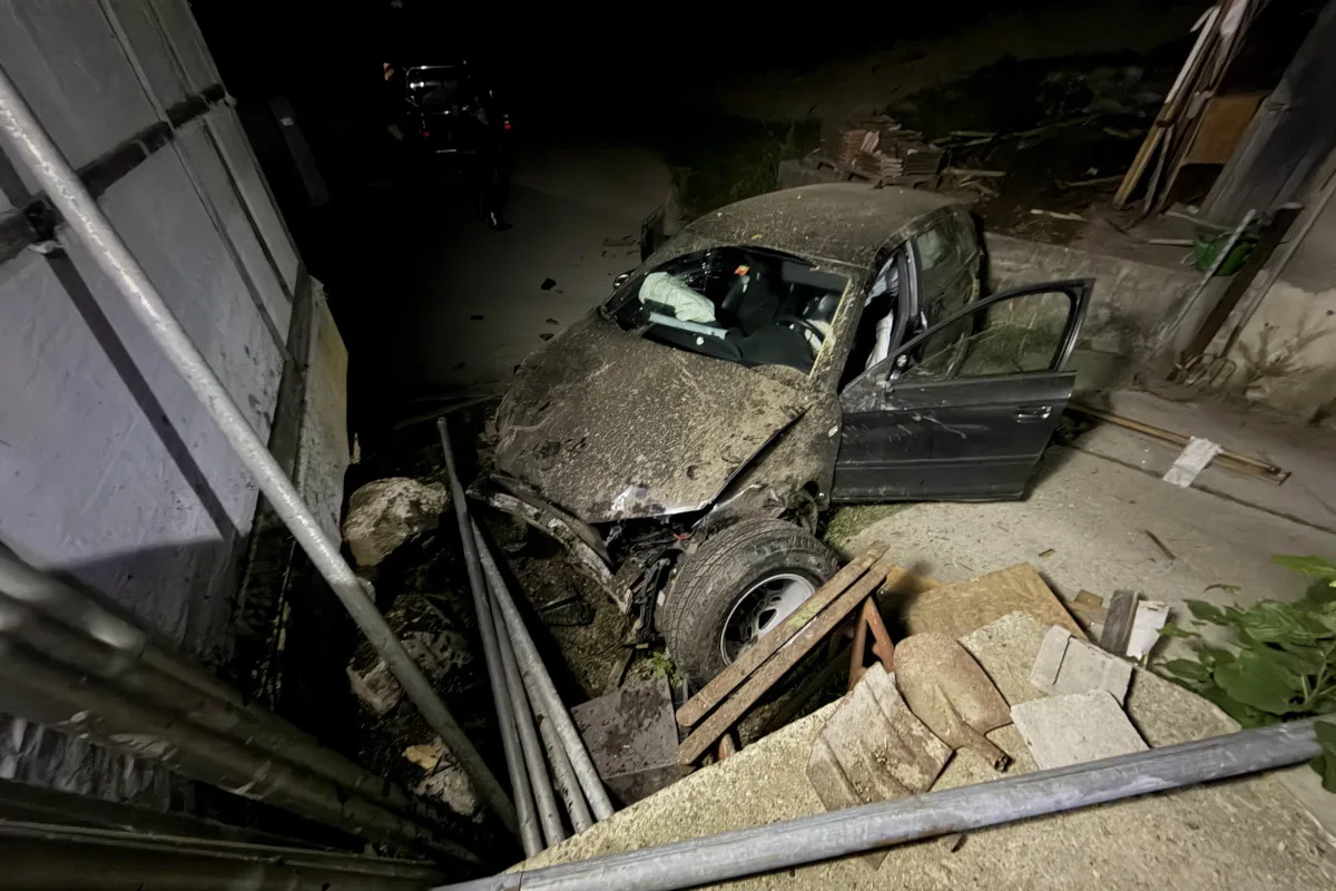 Bei Nacht sieht man ein stark beschädigtes Auto, das in eine Hauswand gefahren ist. Trümmer und Schutt sind sichtbar.