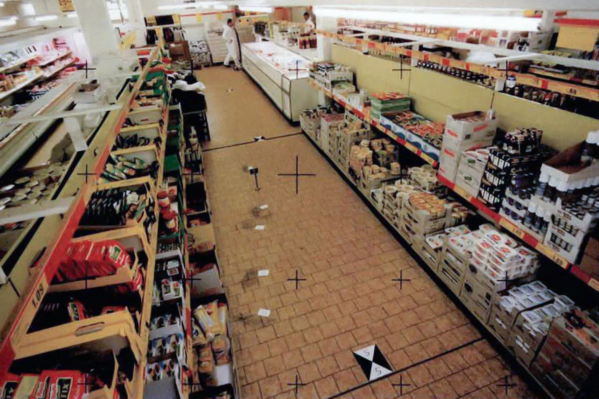 Ein leerer Supermarktgang zeigt mehrere markierte Stellen auf dem Boden, vermutlich Tatortspuren. Im Hintergrund stehen Warenregale.