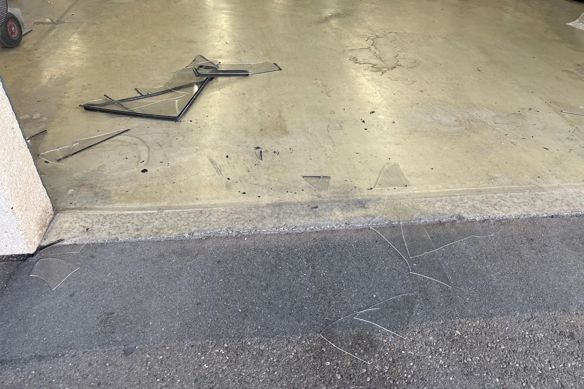 Scherben und Rahmenfragmente liegen verstreut auf einem Garagenboden, teilweise auch auf dem angrenzenden Asphalt.
