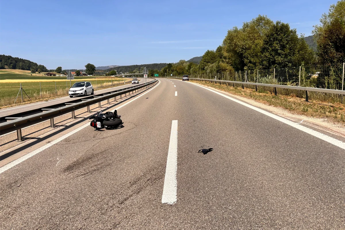 Ein umgefallenes Motorrad liegt auf der rechten Fahrspur einer leeren Landstraße. Der Himmel ist klar, und umliegende Bäume und Felder sind sichtbar.