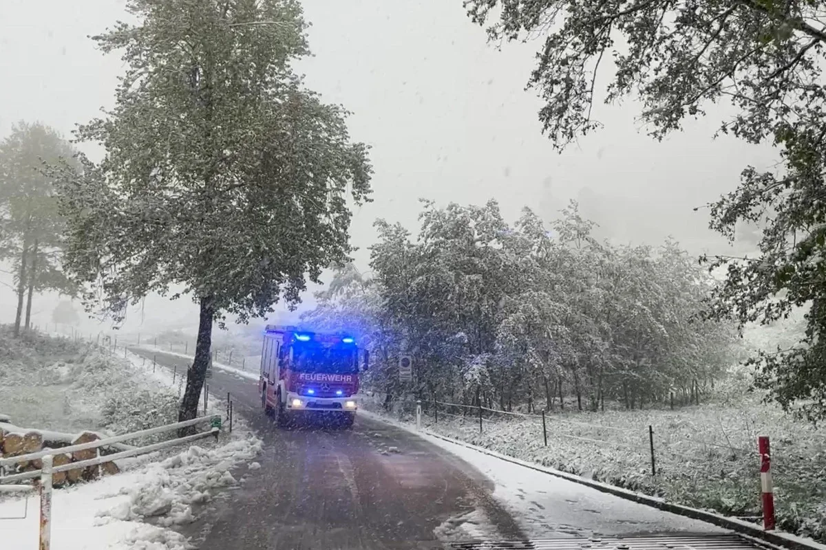Ein Feuerwehrauto fährt eine schneebedeckte Straße entlang. Im Hintergrund sind Bäume mit Schnee bedeckt.