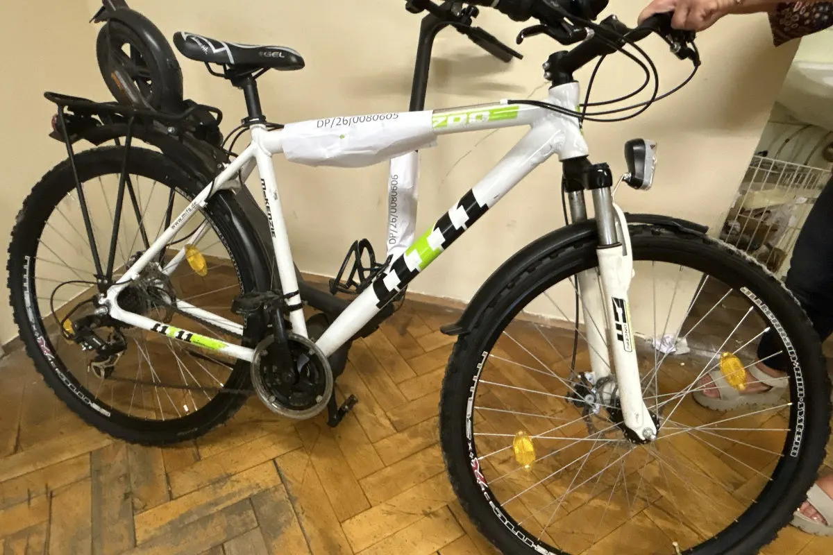 Ein weißes Fahrrad mit schwarz-grünen Akzenten steht in einem Innenraum. Es trägt eine Papiermarkierung am Rahmen.