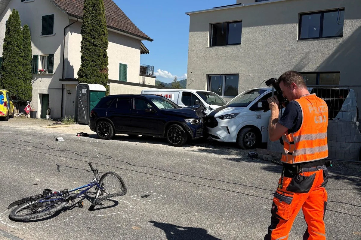 Auf der Straße liegt ein umgestürztes Fahrrad, daneben sind ein schwarzer SUV und ein weißer Transporter zu sehen, die kollidiert sind. Ein Polizist dokumentiert die Szene mit einer Kamera.
