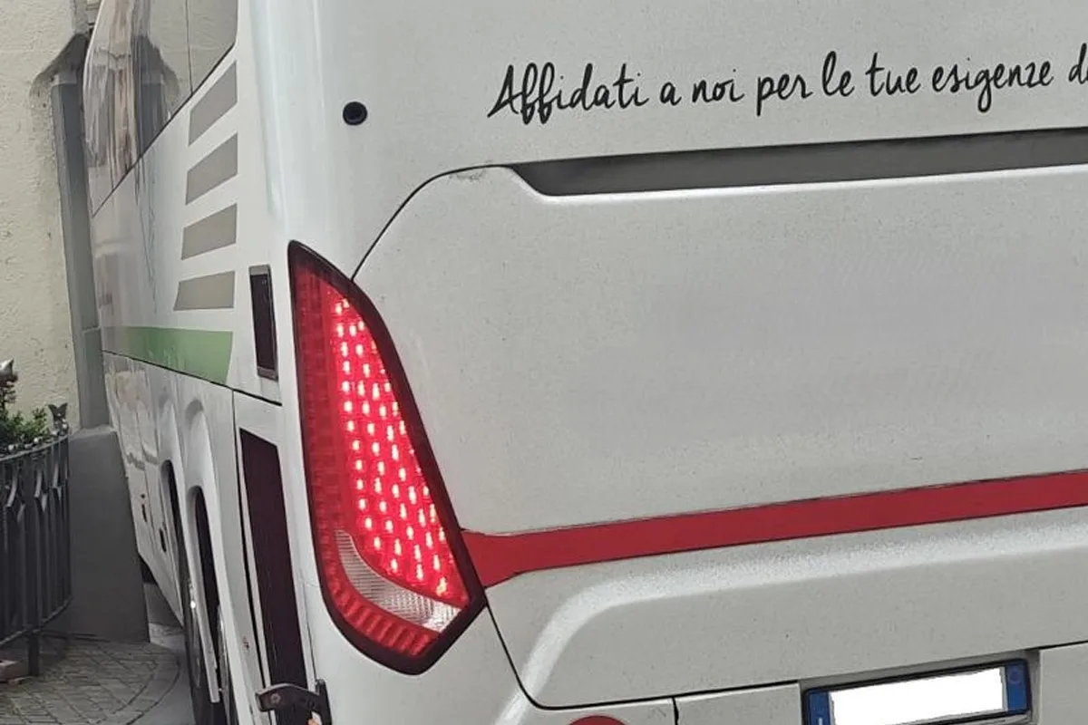 Das Heck eines weißen Busses mit Rücklichtern ist zu sehen, der sich nahe an einer Wand befindet. Italienischer Schriftzug ist sichtbar.