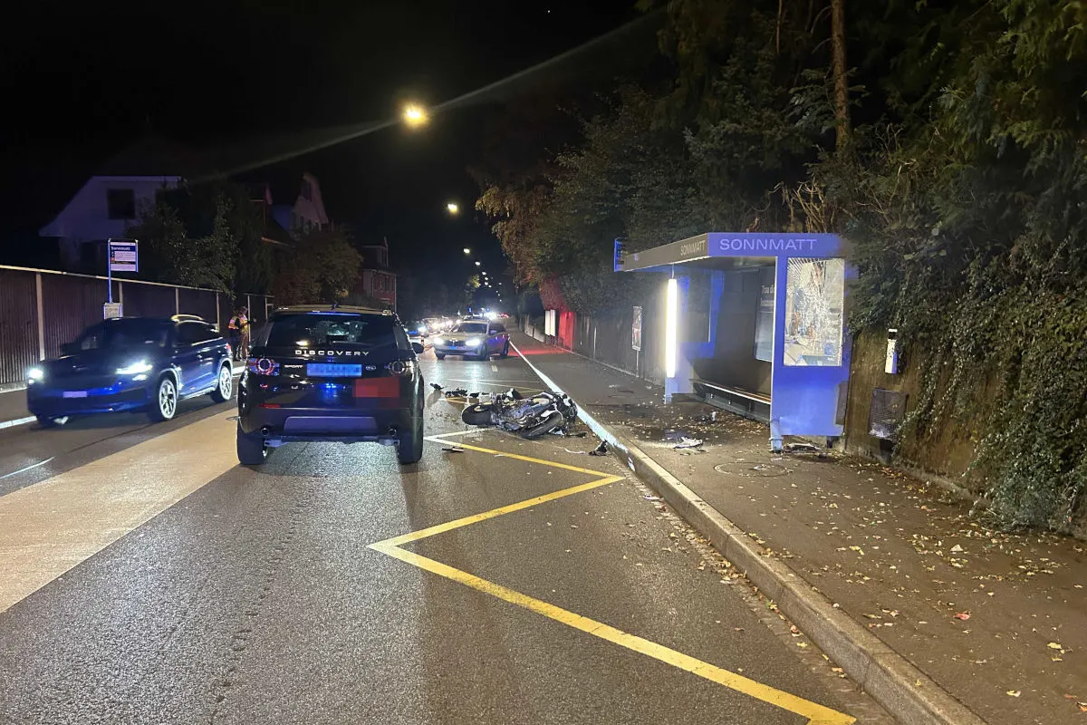 Ein verunfalltes Motorrad liegt auf der Straße neben einer Bushaltestelle mit dem Namen 'Sonnmatt'. Polizeifahrzeuge sind vor Ort.