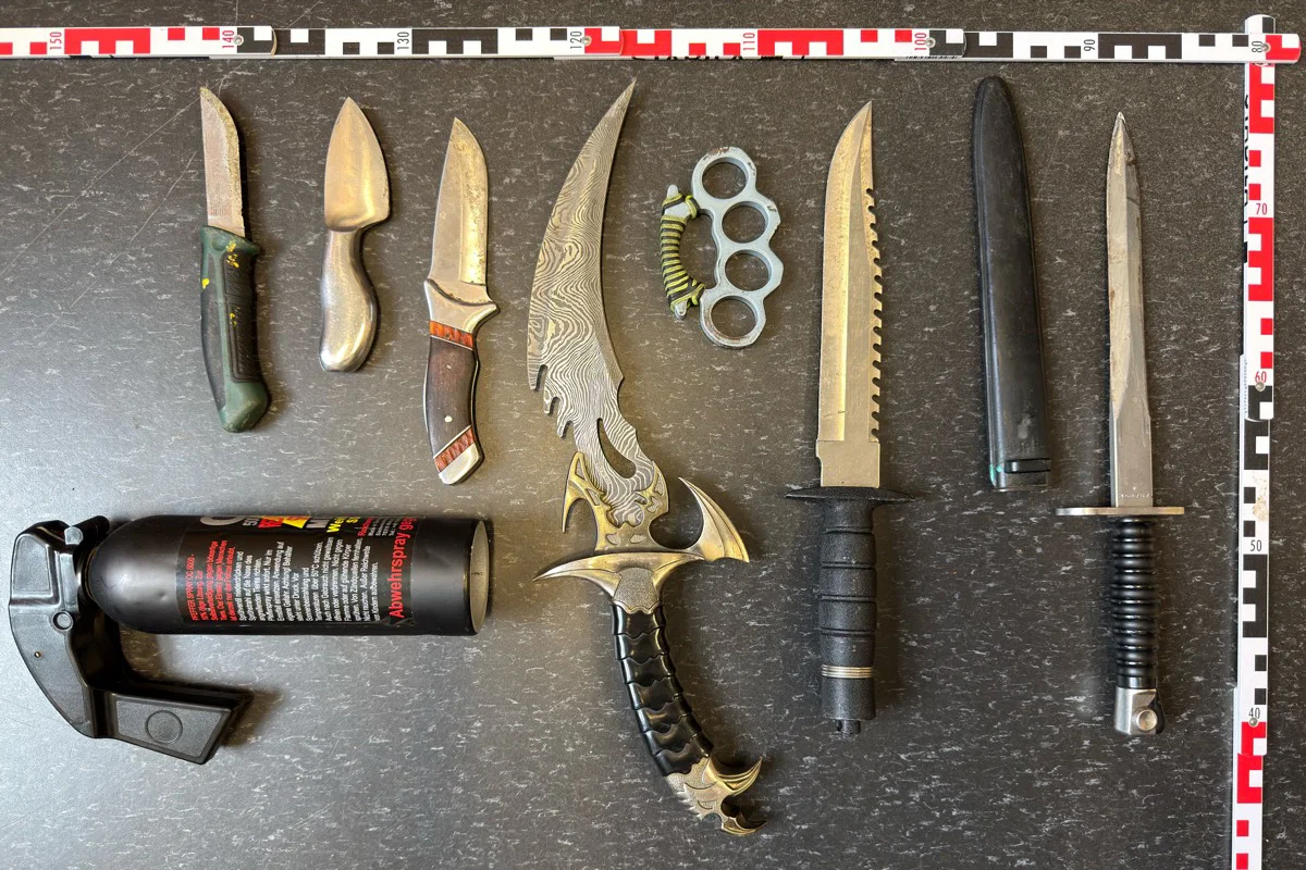 Verschiedene Messer, ein Schlagring und eine Spraydose liegen auf einem Tisch. Ein Maßbandrahmen ist sichtbar.