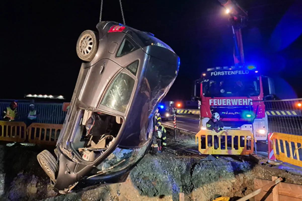 Nachtszene zeigt ein Auto, das von einem Kran aus einer Grube gehoben wird. Feuerwehrkräfte sind im Einsatz.