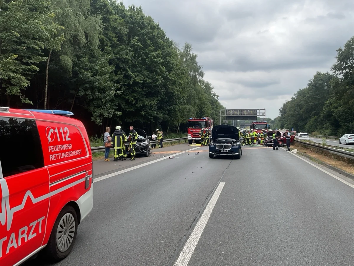 Auf einer Autobahn stehen ein rotes Rettungsfahrzeug, Feuerwehrleute und ein Unfallwagen im Zentrum. Der Verkehr ist unterbrochen.