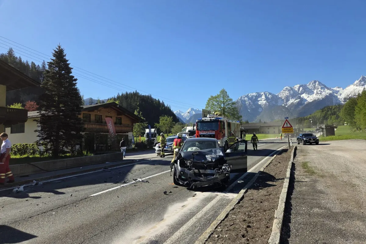 Ein beschädigtes Auto steht auf einer Landstraße in einer alpinen Region. Feuerwehrleute und weitere Einsatzkräfte sind vor Ort.