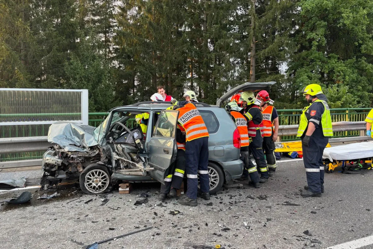 Mehrere Feuerwehrleute arbeiten an einem stark beschädigten Fahrzeug, um eine eingeklemmte Person zu befreien. Eine Trage ist bereitgestellt.