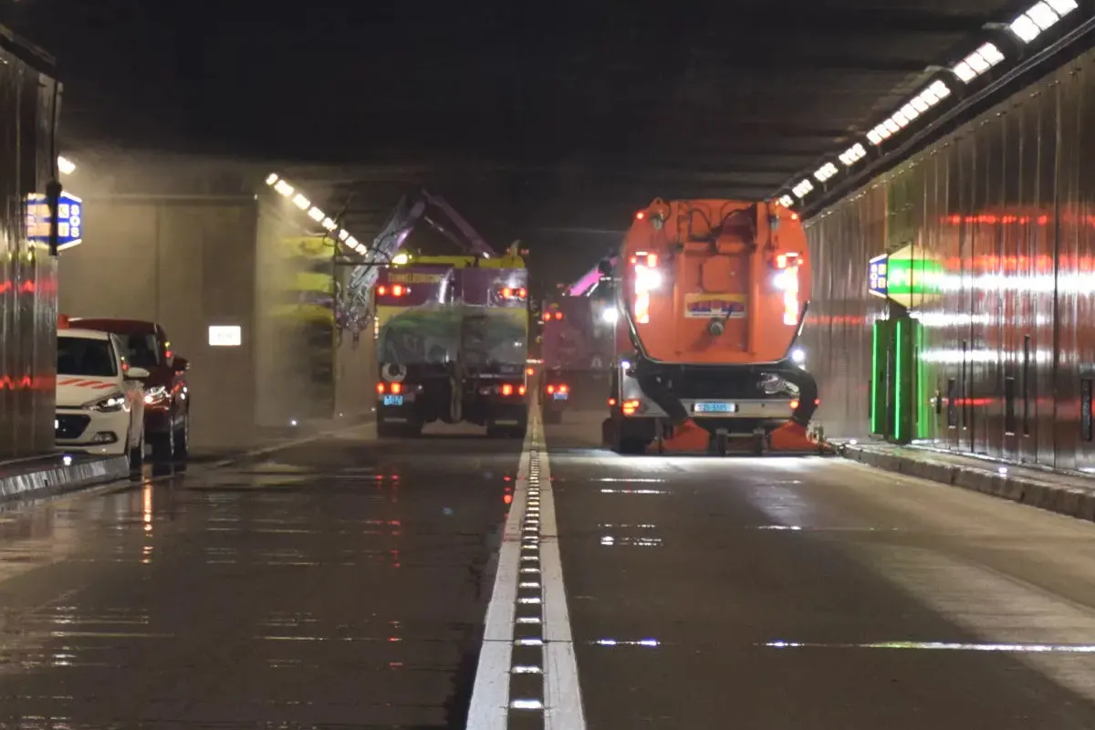 In einem beleuchteten Tunnel sind mehrere Reinigungsfahrzeuge bei der Arbeit. Die Wände sind mit Lichtleisten ausgestattet.