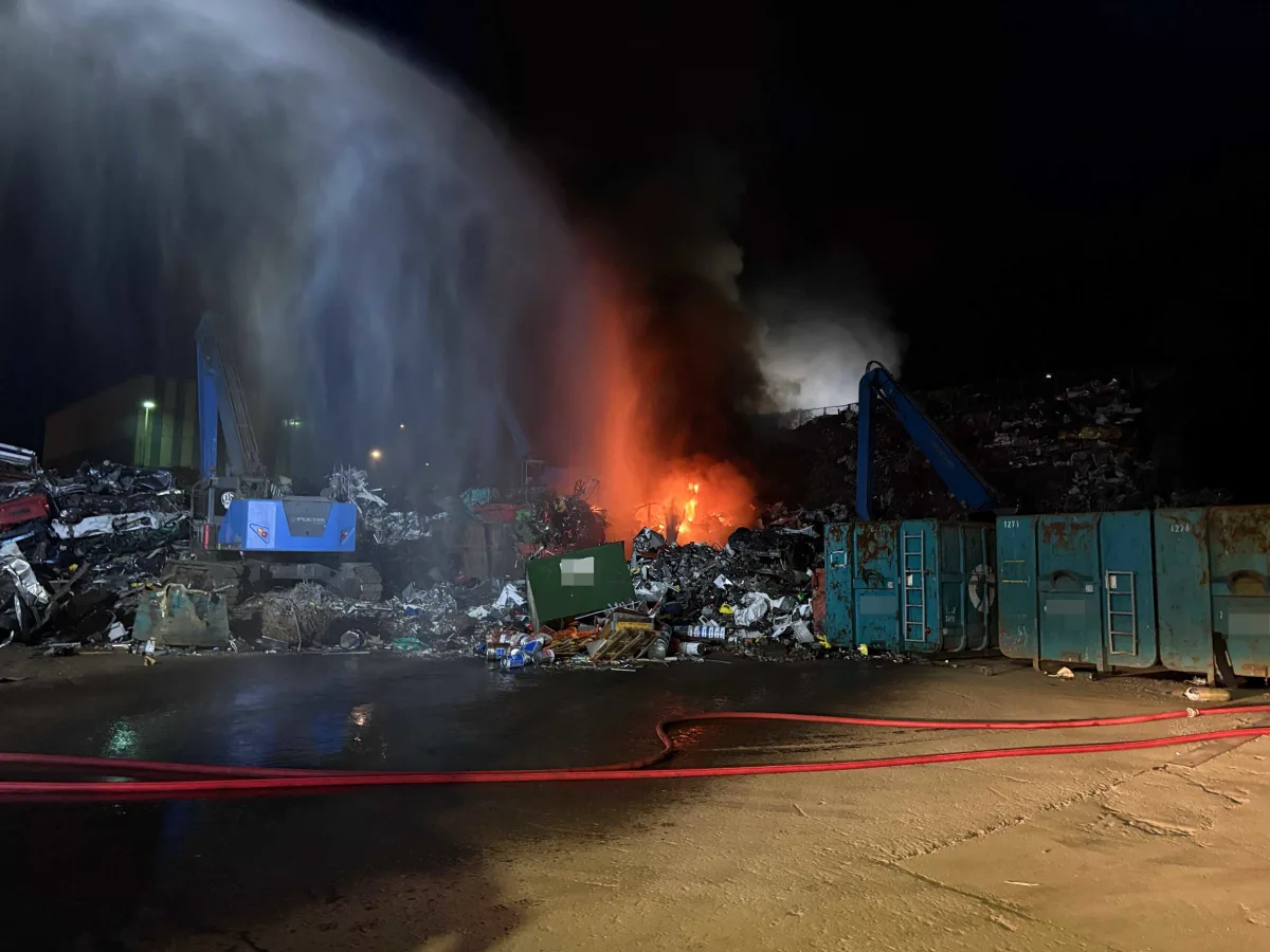 Ein intensiver Brand auf einem Schrottplatz; Feuerwehr löscht das Feuer mit einem Wasserstrahl.