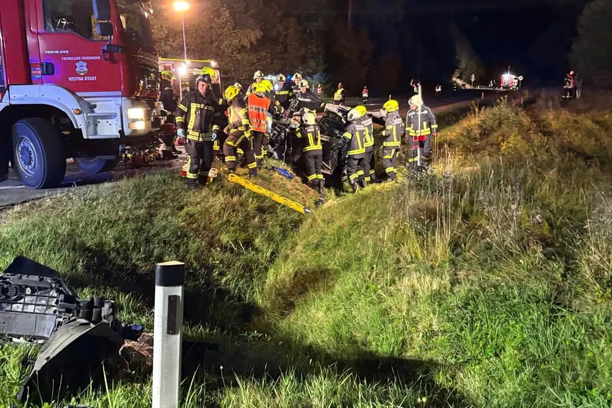 Mehrere Feuerwehrleute in Schutzkleidung arbeiten bei Nacht an einer Unfallstelle auf einer Böschung neben einer Landstraße. Ein Feuerwehrfahrzeug ist sichtbar.