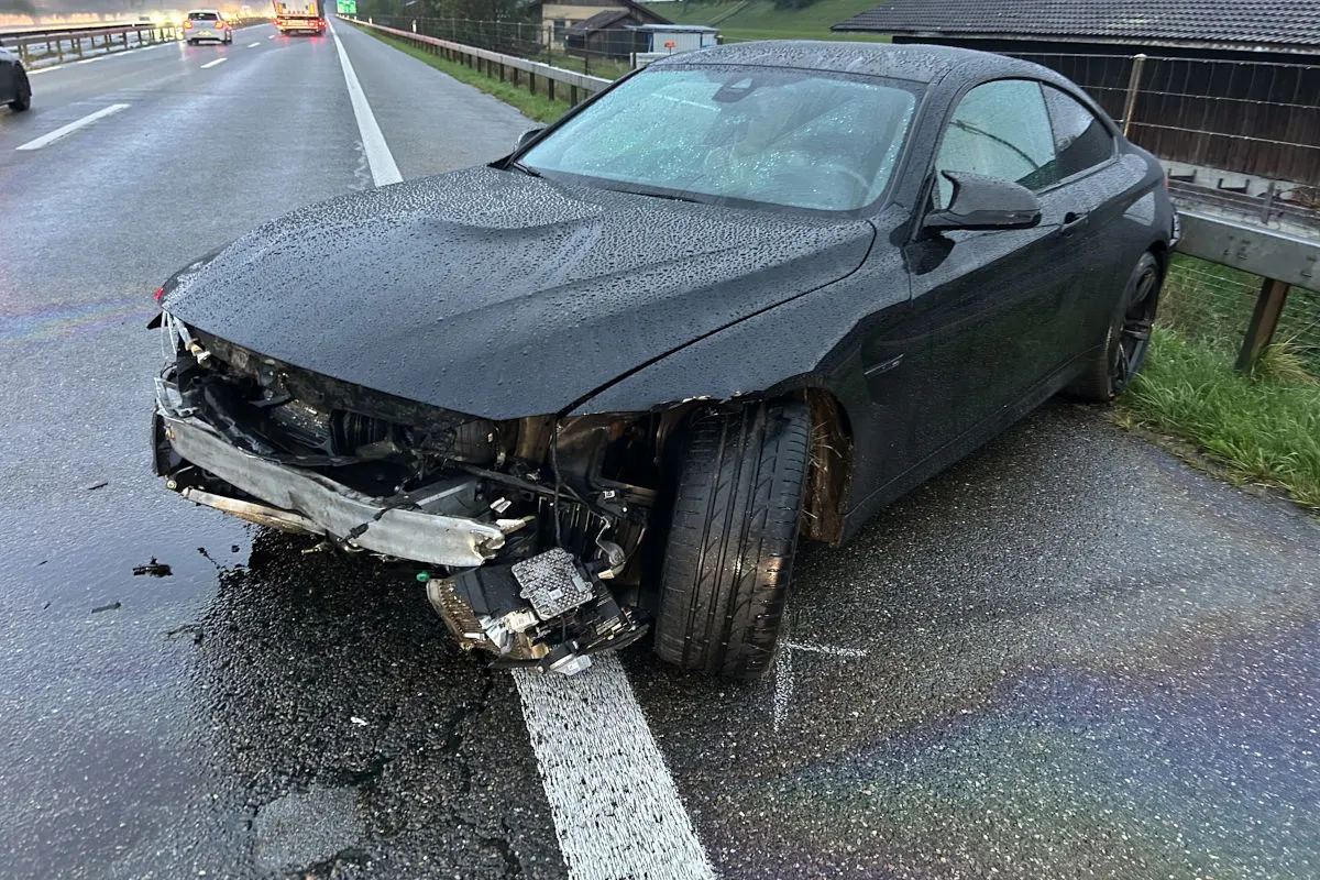 Ein schwarzes Auto mit schweren Frontschäden steht auf einer nassen Autobahn am Fahrbahnrand. Die Frontschürze ist stark beschädigt.