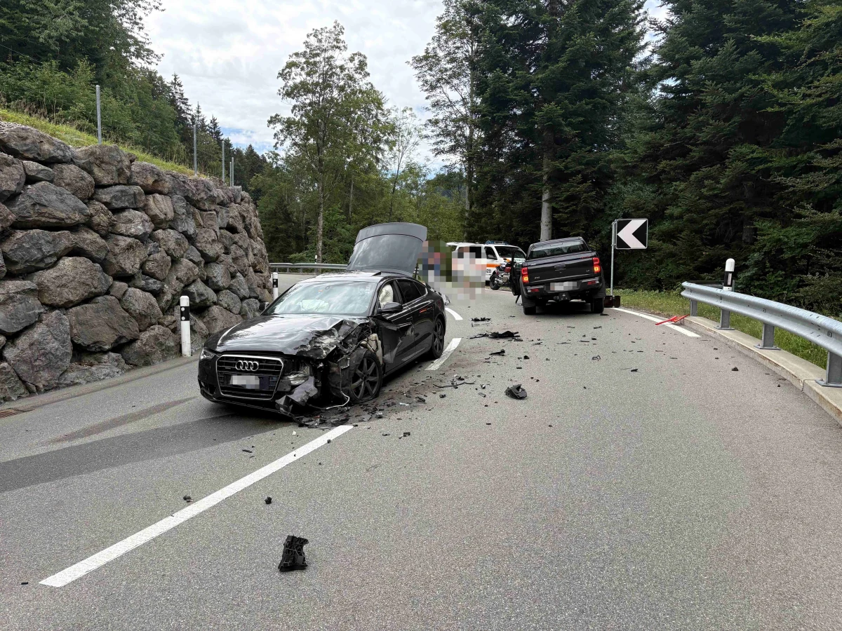 Auf einer Landstraße stehen ein beschädigter schwarzer Audi und ein weiteres Fahrzeug nach einem Unfall. Trümmerteile sind auf der Straße verteilt.