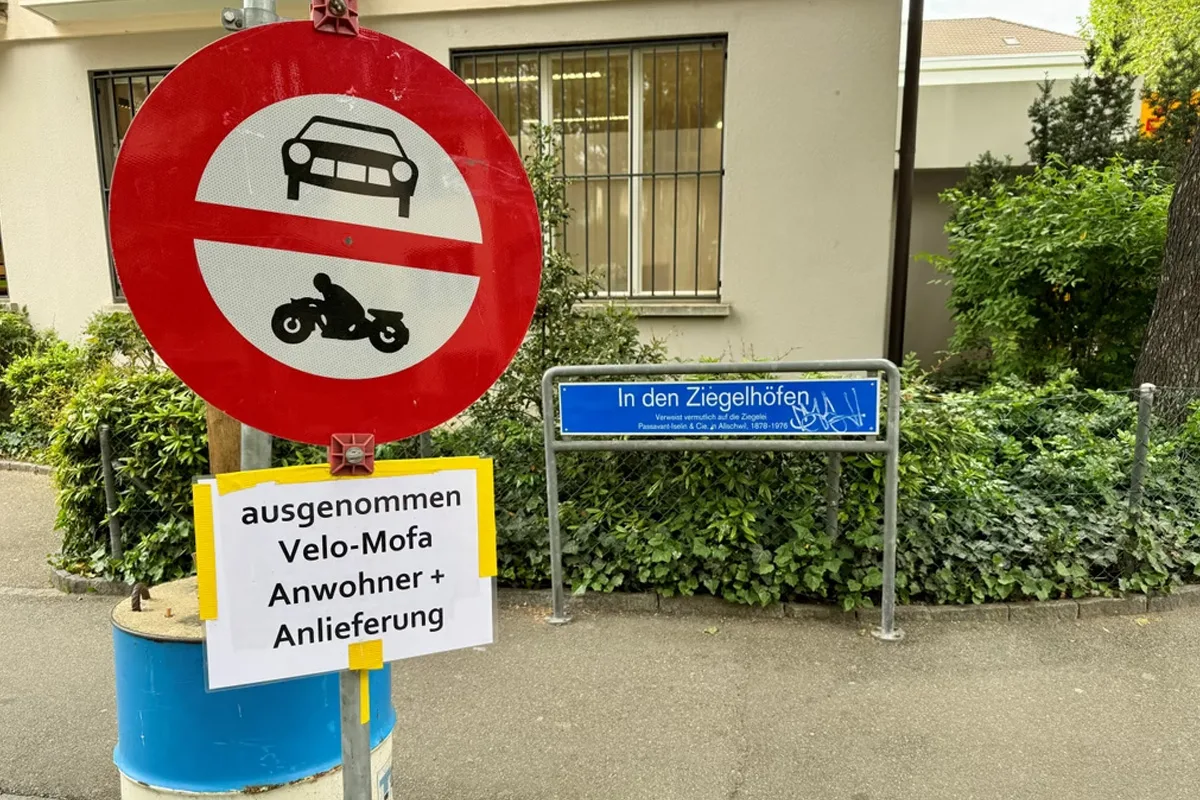 Ein Verkehrsschild zeigt ein Durchfahrtsverbot für Autos und Motorräder. Darunter steht ein Schild: 'ausgenommen Velo-Mofa, Anwohner + Anlieferung'.