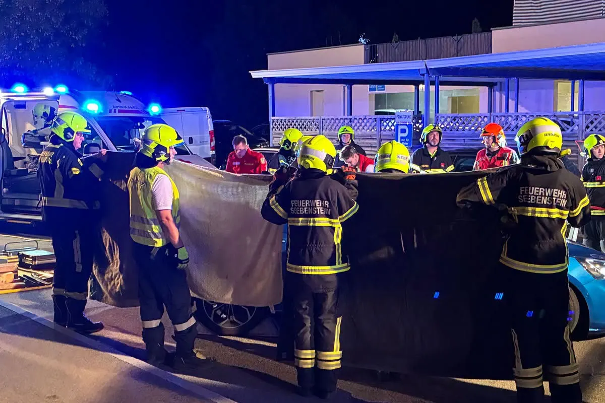 Mehrere Feuerwehrleute der Feuerwehr Seebenstein halten bei Nacht einen Sichtschutz an einer Unfallstelle. Im Hintergrund sind weitere Einsatzkräfte und ein Rettungswagen zu sehen.