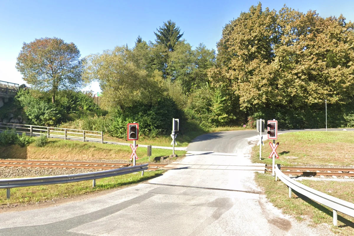 Ein Bahnübergang mit Schranken, Verkehrszeichen und Eisenbahnschienen in einer ländlichen Umgebung.