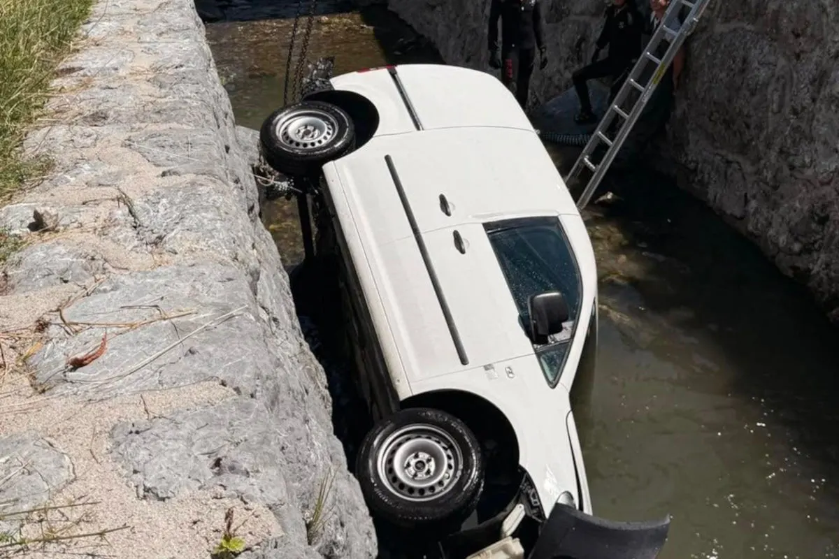 Ein weißer Transporter liegt in einem schmalen Wassergraben und wird mit einer Kette und Leiter geborgen. Personen stehen am Rand.