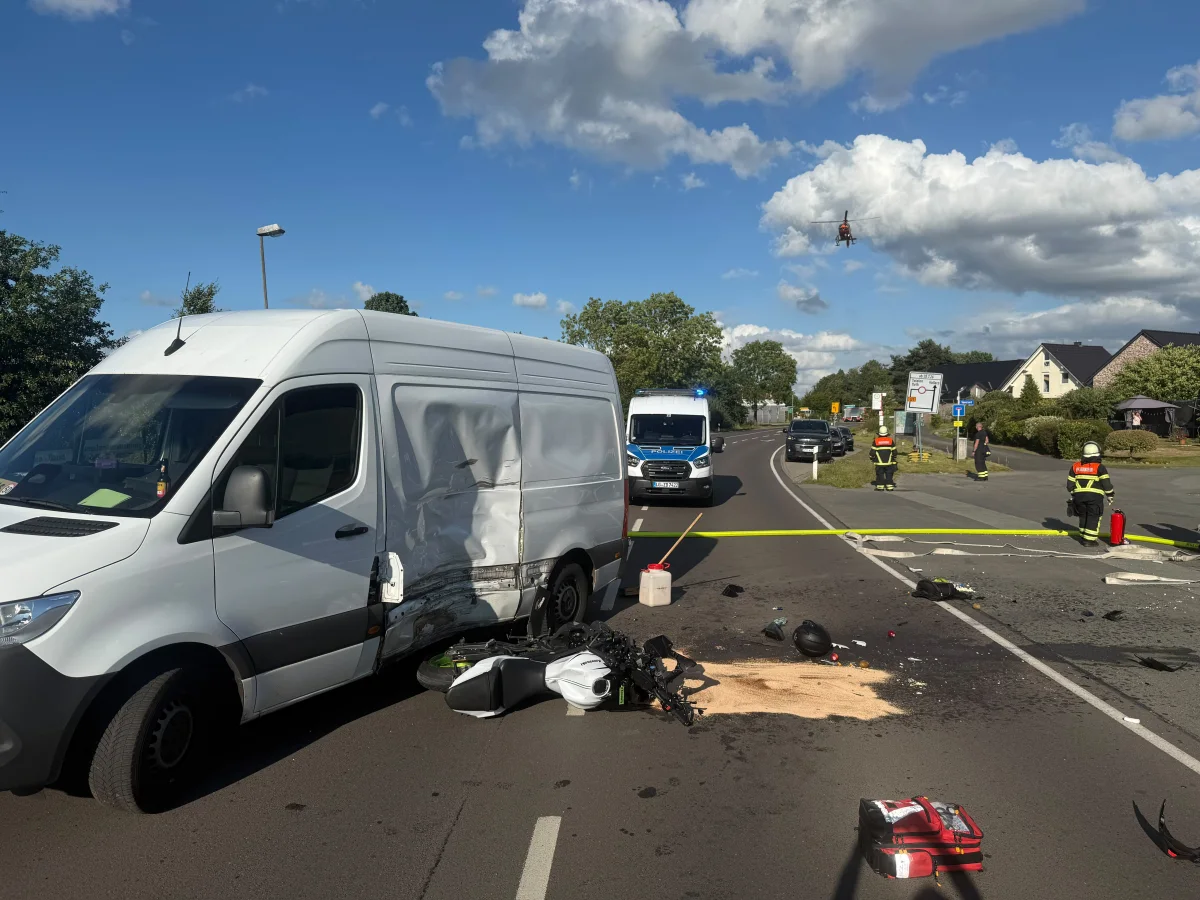 Ein weißer Lieferwagen mit Unfallspuren steht auf einer Straße, daneben liegt verstreutes Zubehör. Rettungskräfte sind vor Ort.