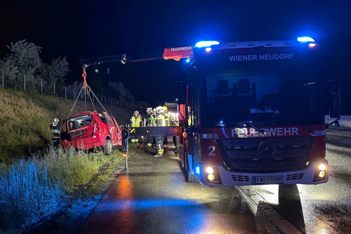 Bei Nacht wird ein rotes Fahrzeug von der Feuerwehr Wiener Neudorf mit einem Kran von der Straße geborgen. Mehrere Feuerwehrleute sind im Einsatz.