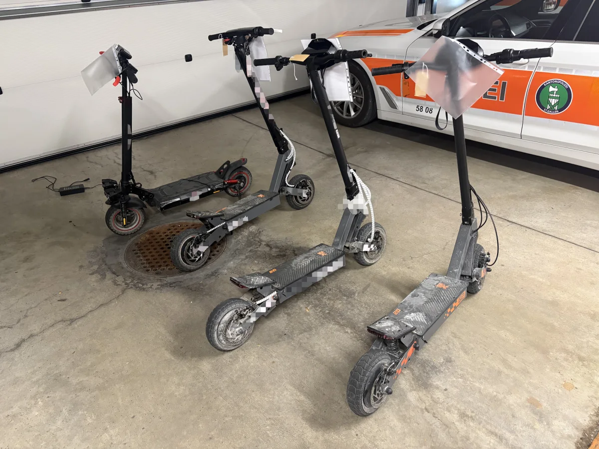 Mehrere E-Scooter, die in einer Garage abgestellt sind, befinden sich vor einem Polizeiauto. Diese Fahrzeuge scheinen beschlagnahmt worden zu sein.