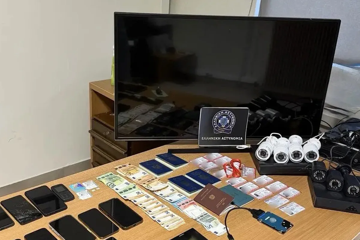 Auf einem Tisch liegen beschlagnahmte Handys, Geldscheine, Ausweise und Überwachungskameras. Ein Polizeiwappen ist sichtbar.