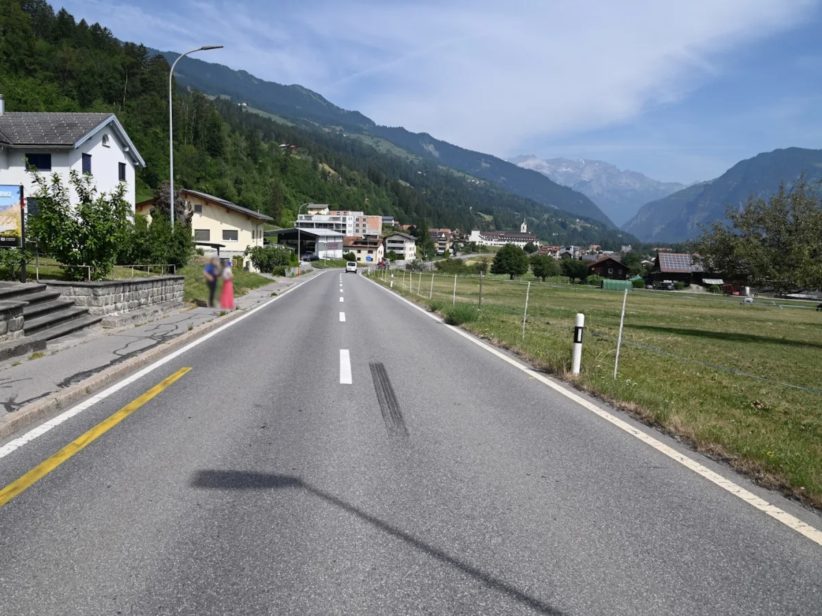 Eine Landstraße führt durch eine ländliche Gegend mit Bergen im Hintergrund. Auf der Straße sind Bremsspuren sichtbar.