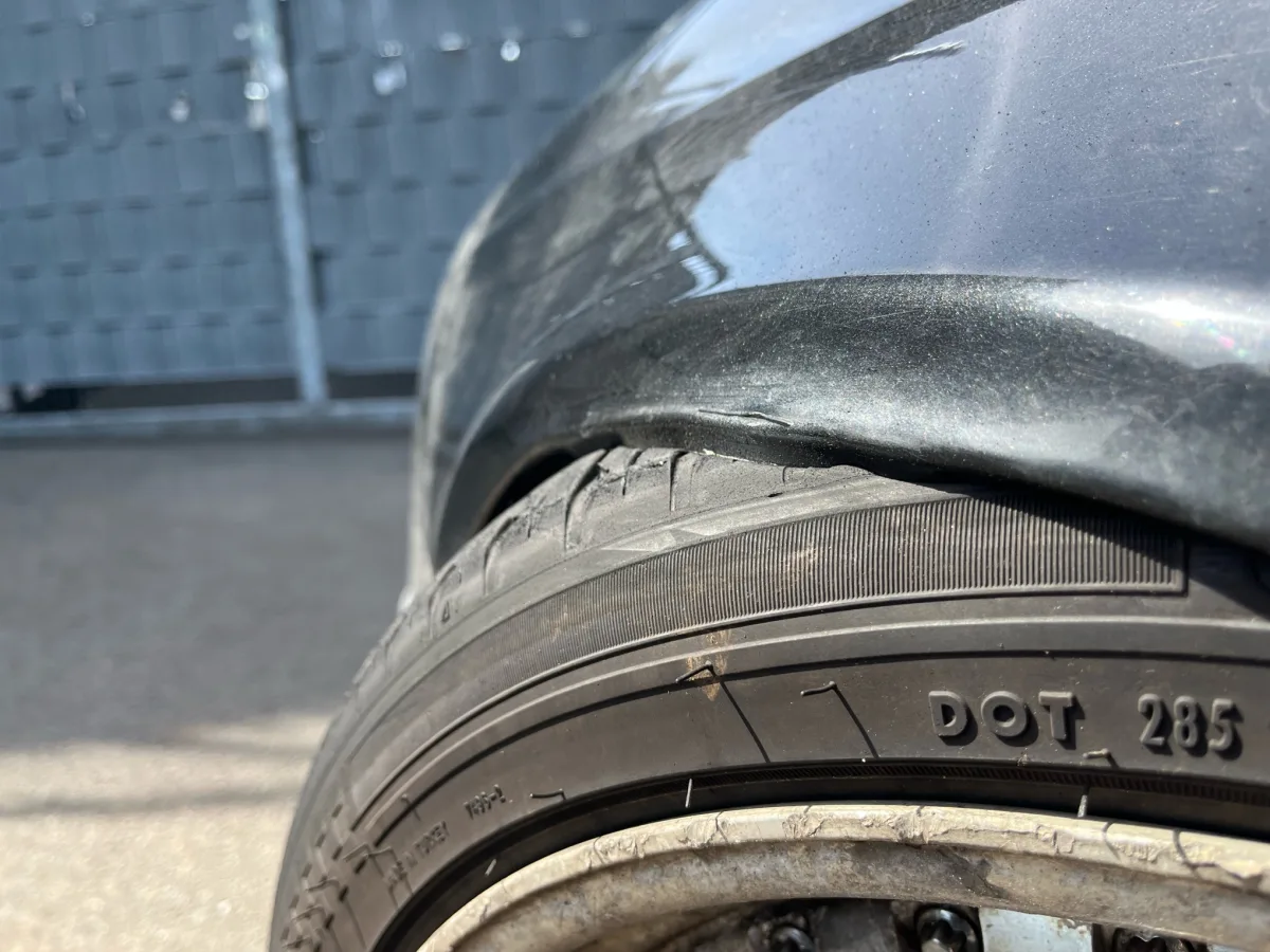 Nahaufnahme eines Autos, das einen beschädigten Kotflügel und einen Reifen zeigt. Es sind Kratzer und Verformungen erkennbar.
