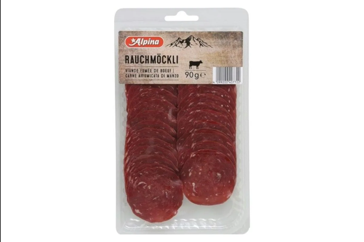 Die Abbildung zeigt eine durchsichtige Plastikverpackung mit geschnittenem Rauchmöckli der Marke Alpina. Das Etikett oben ist sichtbar und beschreibt das Produkt.