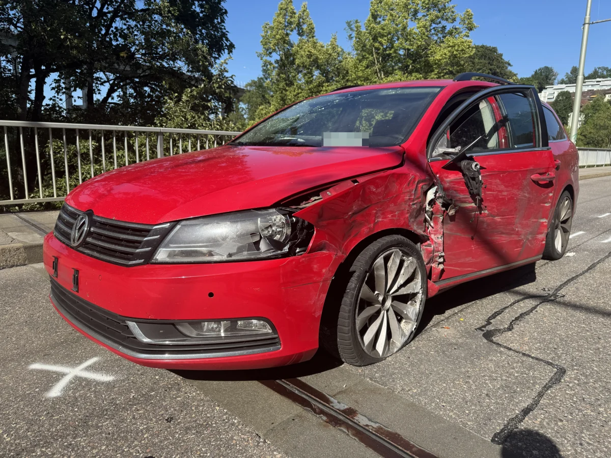 Ein roter VW mit eingedrückter Fahrerseite steht auf einer Straße. Die Front- und Seitenscheibe sind unbeschädigt.