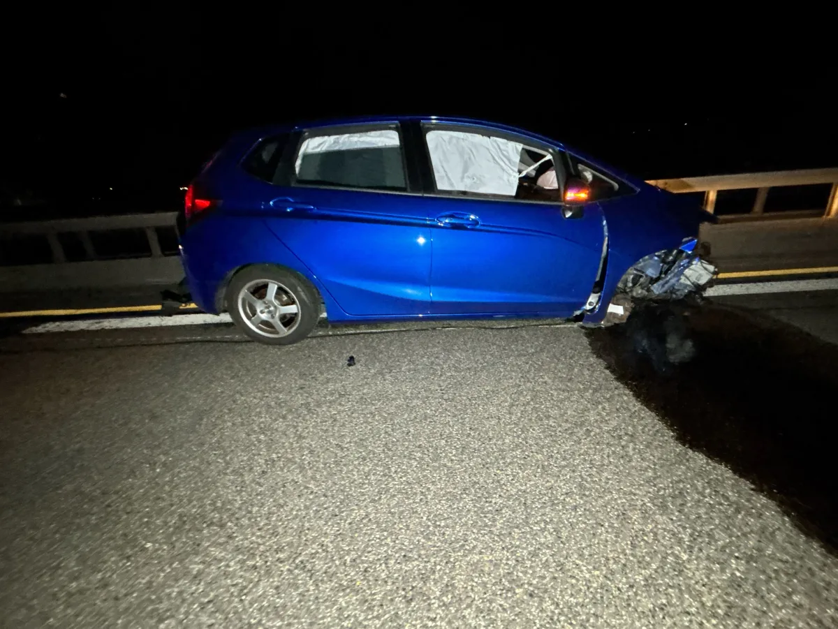 Ein blaues Auto zeigt erheblichen Frontschaden nach einem Unfall. Es steht auf einer unbeleuchteten Straße bei Nacht.