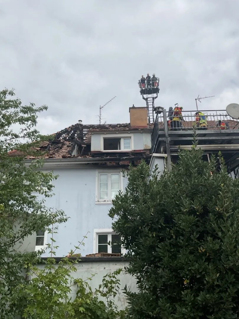 Ein Haus mit erheblich beschädigtem Dach, Feuerwehrleute stehen auf einer Hebebühne und begutachten den Schaden.