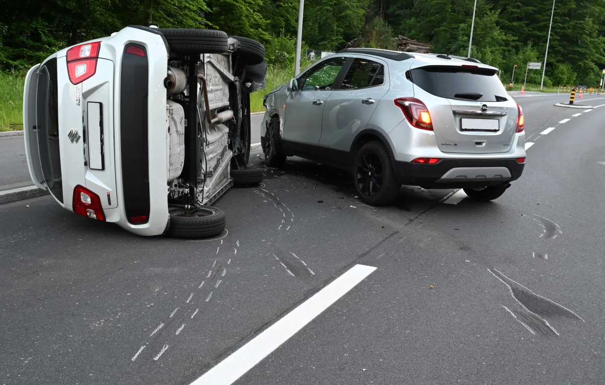 Ein weißes Auto liegt nach einem Unfall auf der Seite, während ein silberner SUV daneben beschädigt auf einer Straße steht. Reifenspuren sind auf dem Asphalt sichtbar.