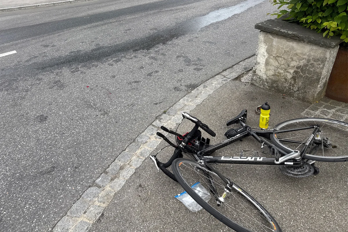 Ein umgestürztes Fahrrad liegt auf dem Gehweg neben einer gelben Wasserflasche, nahe der Straße.