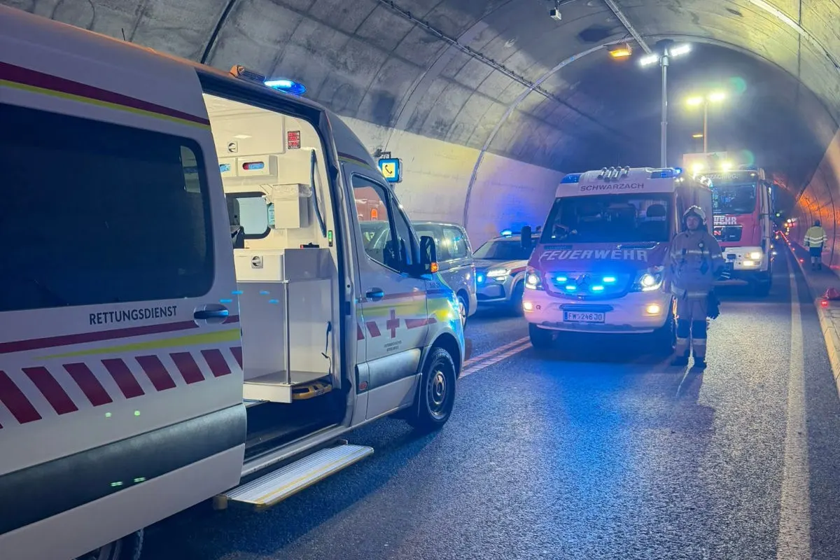 Ein Rettungsdienstfahrzeug und mehrere Feuerwehrfahrzeuge stehen in einem Tunnel mit aktivem Blaulicht, Einsatzkräfte sind sichtbar.