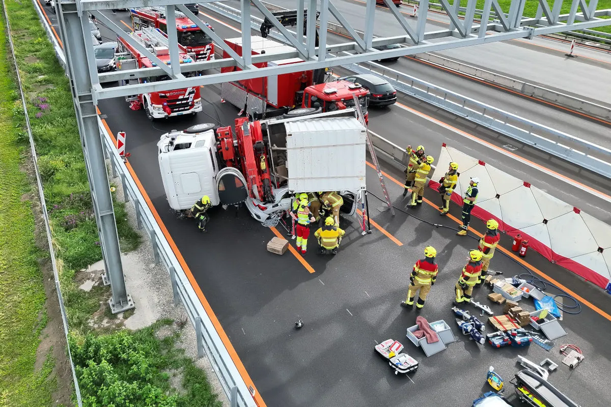 Mehrere Rettungskräfte arbeiten um einen umgekippten Lkw auf einer Autobahn herum. Ausrüstung liegt auf der Fahrbahn.