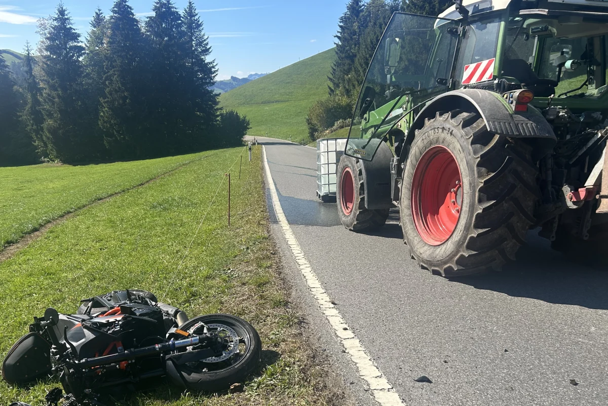 Ein umgestürztes Motorrad liegt auf der Wiese neben einer kurvenreichen Straße. Ein Traktor steht teilweise auf der Fahrbahn.