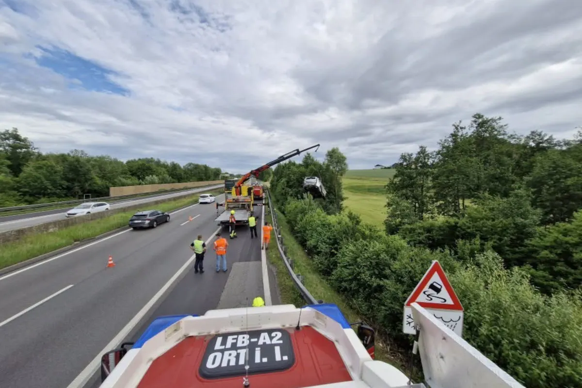 Ein Autokran hebt ein Fahrzeug von einer Böschung entlang einer Autobahn, während mehrere Personen in Warnwesten zuschauen.