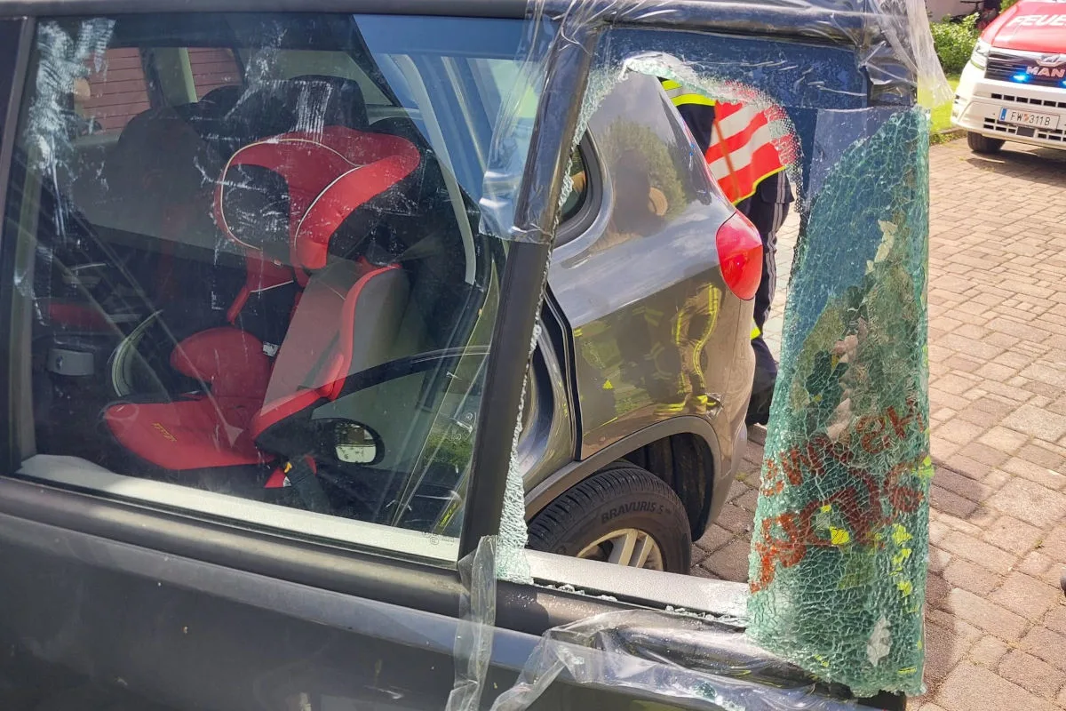 Ein beschädigtes Autofenster zeigt einen roten Kindersitz im Inneren des Fahrzeugs. Das Glas ist zersplittert.