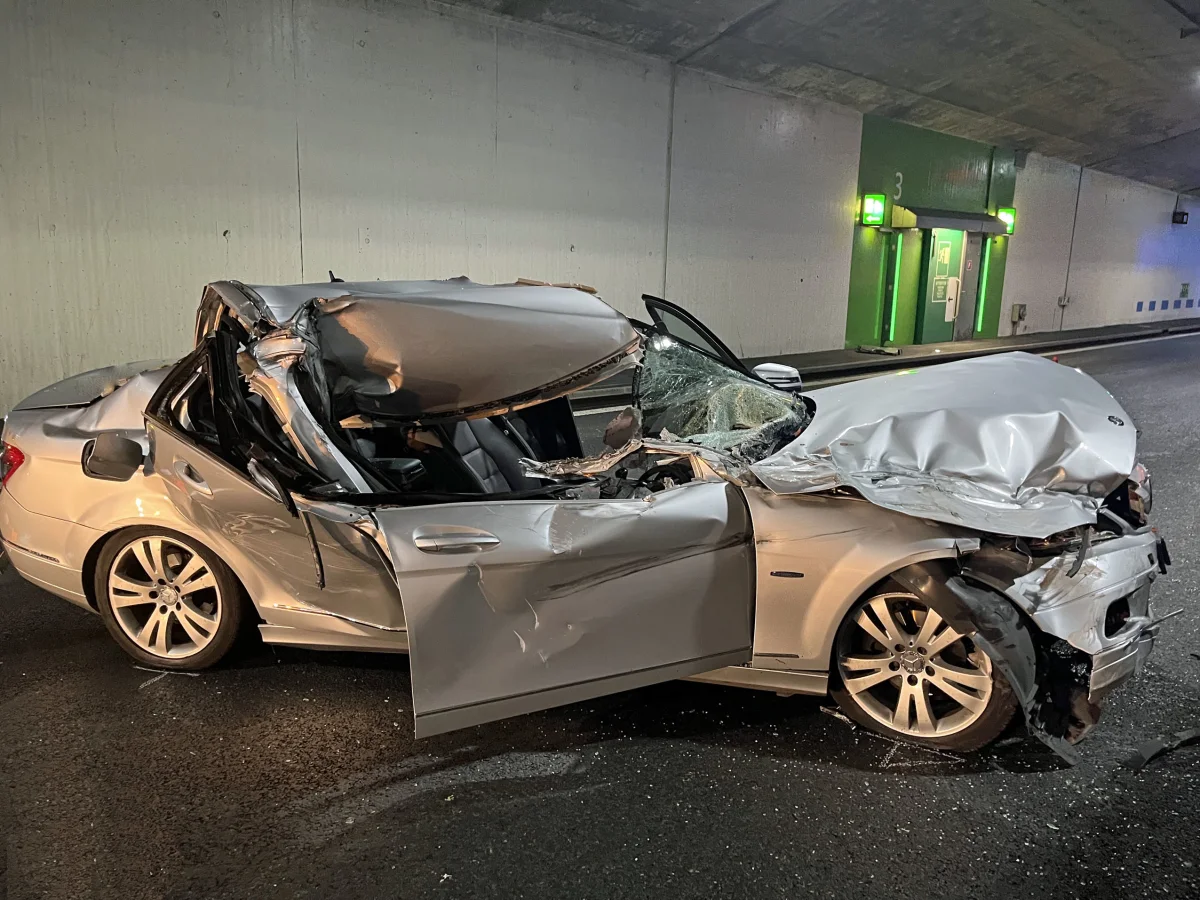 Ein silbernes Auto mit schweren Schäden ist in einem Tunnel zu sehen. Die Front und das Dach sind stark eingedrückt.
