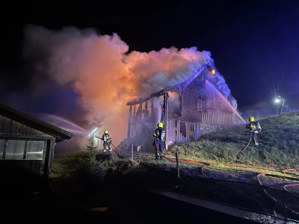 Mehrere Feuerwehrleute kämpfen gegen einen nächtlichen Brand eines großen Gebäudes an. Es sind starke Rauchentwicklungen und Flammen sichtbar.