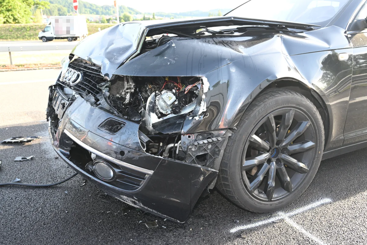 Ein schwarzer Audi steht auf einer Straße mit stark eingedrückter Motorhaube und offenem Scheinwerferbereich, umgeben von Trümmerteilen.