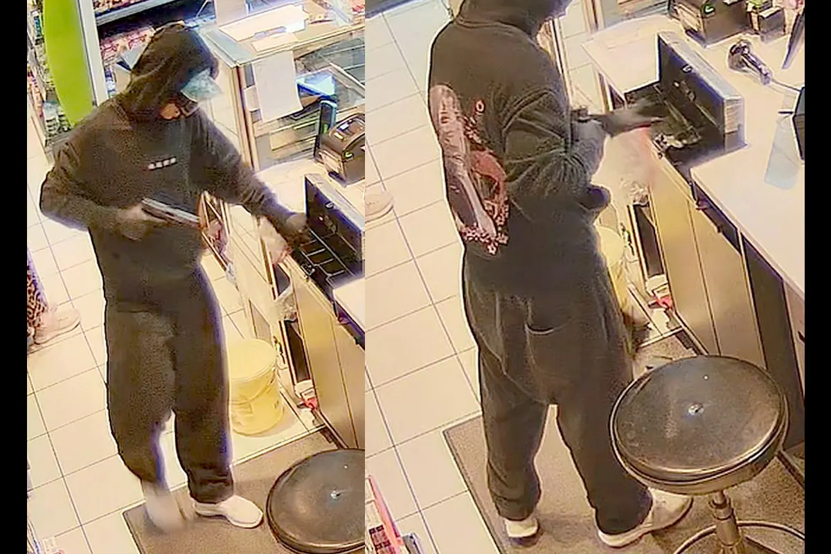 Eine vermummte Person steht in einem Geschäft hinter dem Tresen und öffnet eine Kasse. Das Bild zeigt sie von der Seite im Moment des Zugriffs.