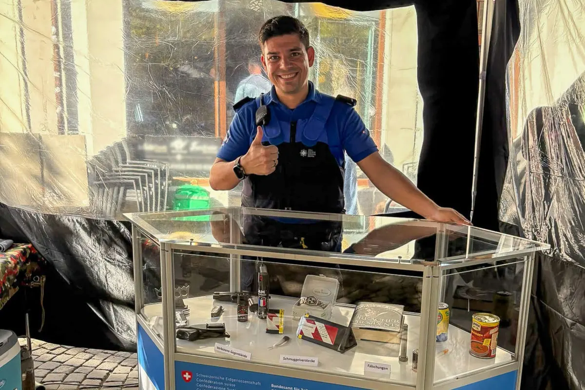 Ein lächelnder Polizist zeigt den Daumen hoch. Vor ihm steht eine Vitrine mit beschlagnahmten Objekten. Verschiedene Gegenstände sind deutlich sichtbar darin.